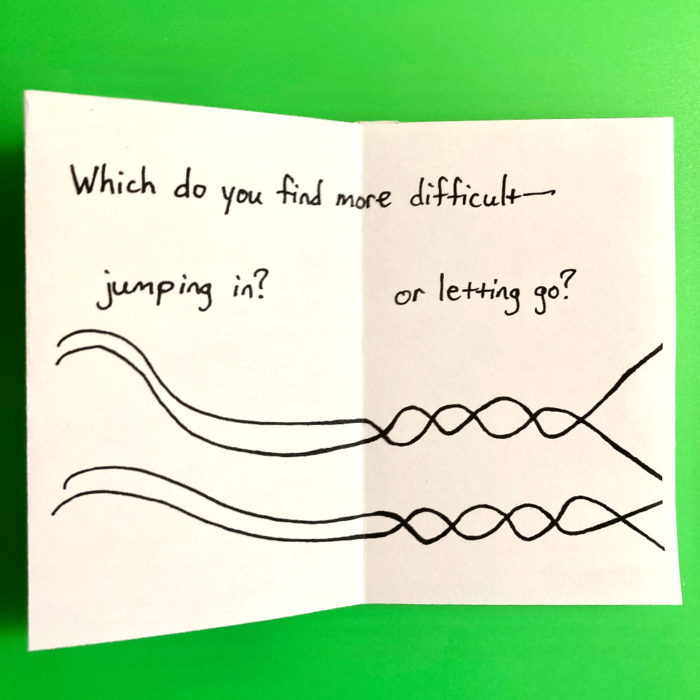 The last two pages of the zine. The text says "Which do you find more difficult--jumping in or letting go?" The zine is printed on white paper with black text and drawings. An illustration on the bottom of the page shows two wavy lines that then intersect into a double-helix. Near the right edge of the page, the lines separate. The background of the photo is green.