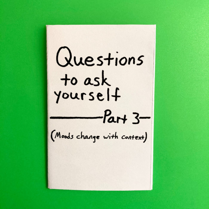 A mini zine titled "Questions to ask yourself: Part 3". The subtitle says "Moods change with context." The zine is printed on white paper with black text. The background of the photo is green.