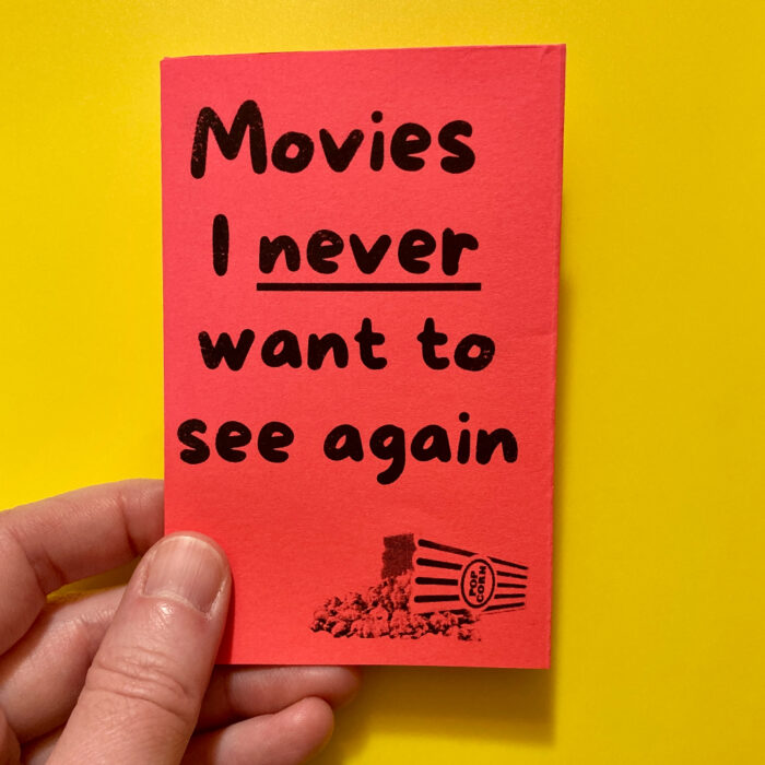 The cover of "Movies I never want to see again." The text is printed in black on red paper. In the bottom right corner, there's a photo of a spilled popcorn bucket.