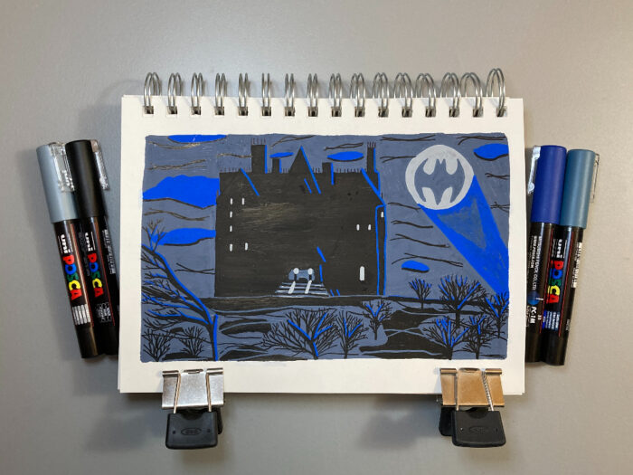 A colored illustration of Bruce Wayne's mansion (Wayne Manor). The building is painted back with blue highlights. Windows are illuminated in white on the left and right sides of the building. To the right of the building, there's a bat symbol in the sky. The sky is painted a cool gray color with blue clouds, and black lines. In front of the building, in the foreground, there are small trees painted in black with blue highlights.