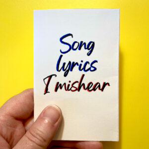 A hand holding the mini zine "Song lyrics I mishear"