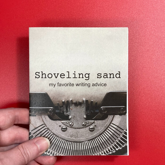 A hand holding the zine "Shoveling sand: My favorite writing advice." The cover of the zine features a close-up photo of a typewriter. The title of the zine is positioned to look as if the typewriter typed the text.