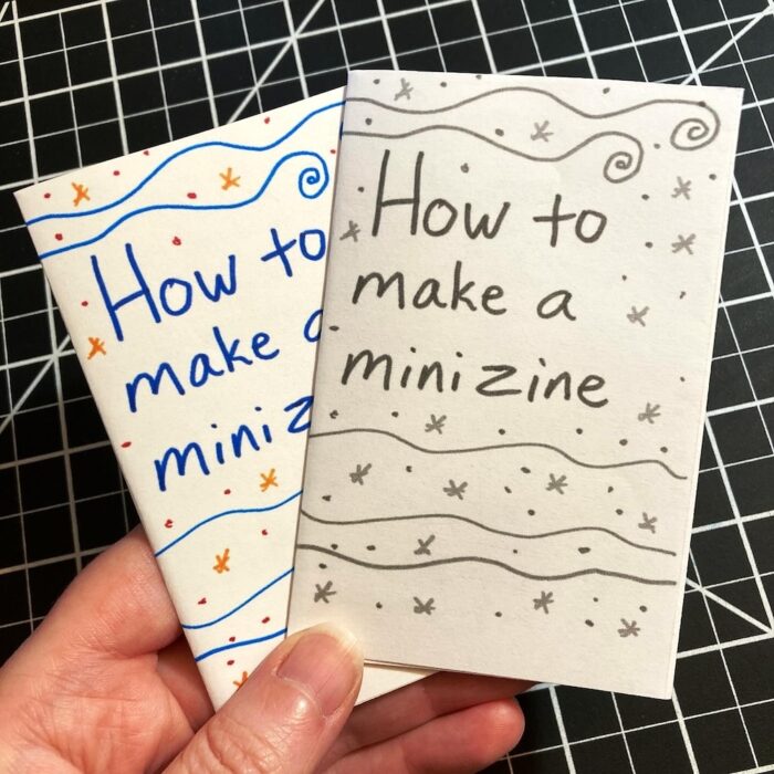 A hand holds mini zines titled, "How to make a mini zine." One version of the zine is in color and the other version is in black and white.