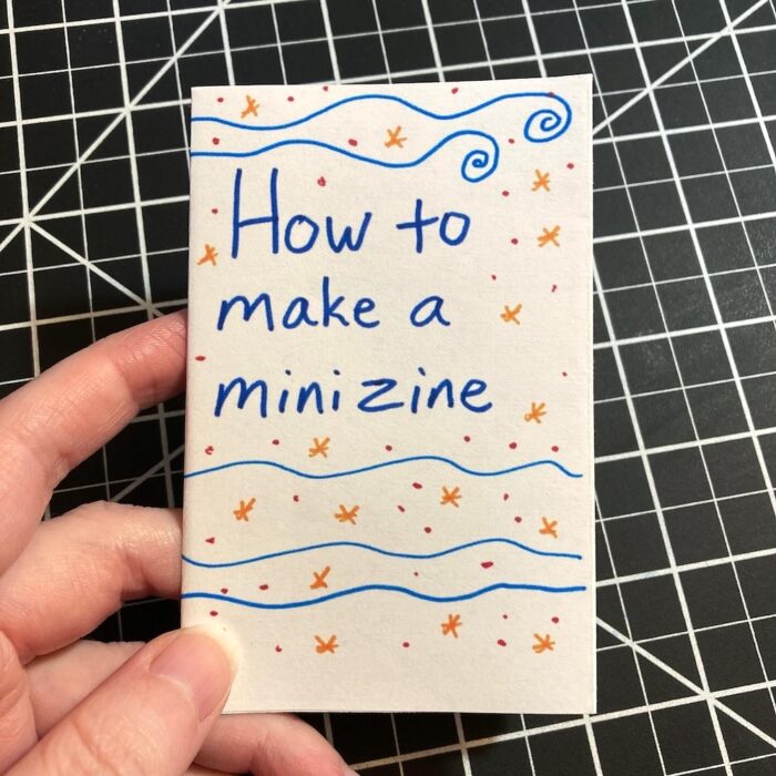 A hand holds a mini zine titled, "How to make a mini zine."